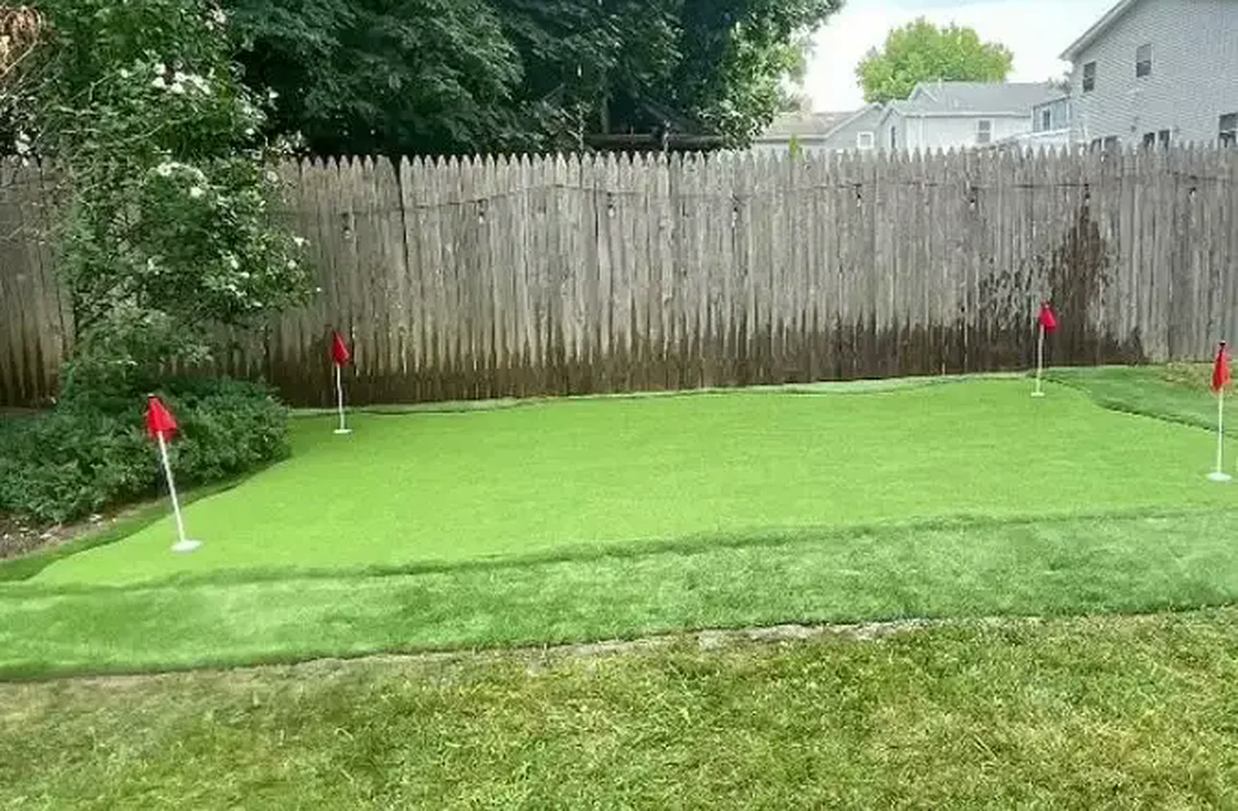 Custom backyard synthetic putting green with five flagged holes installed by Turf Boss Construction