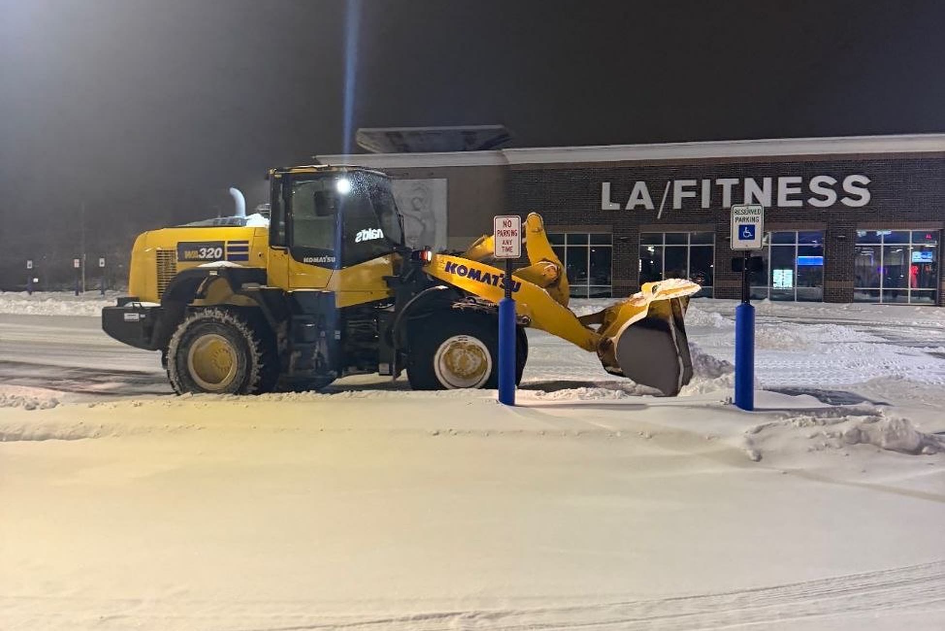 Komatsu WA320 wheel loader clearing a snow-covered commercial parking lot at night during a storm