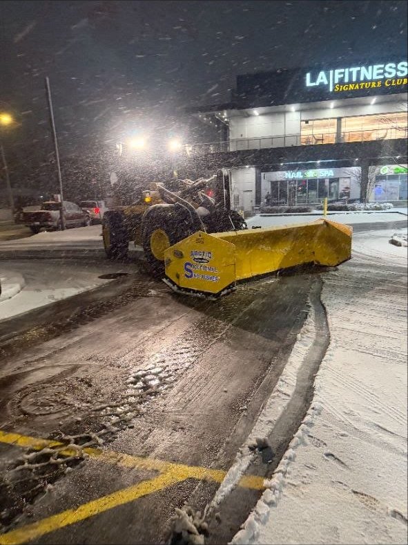 Arctic Sectional Sno-Pusher on a Turf Boss wheel loader clearing a retail lot at night