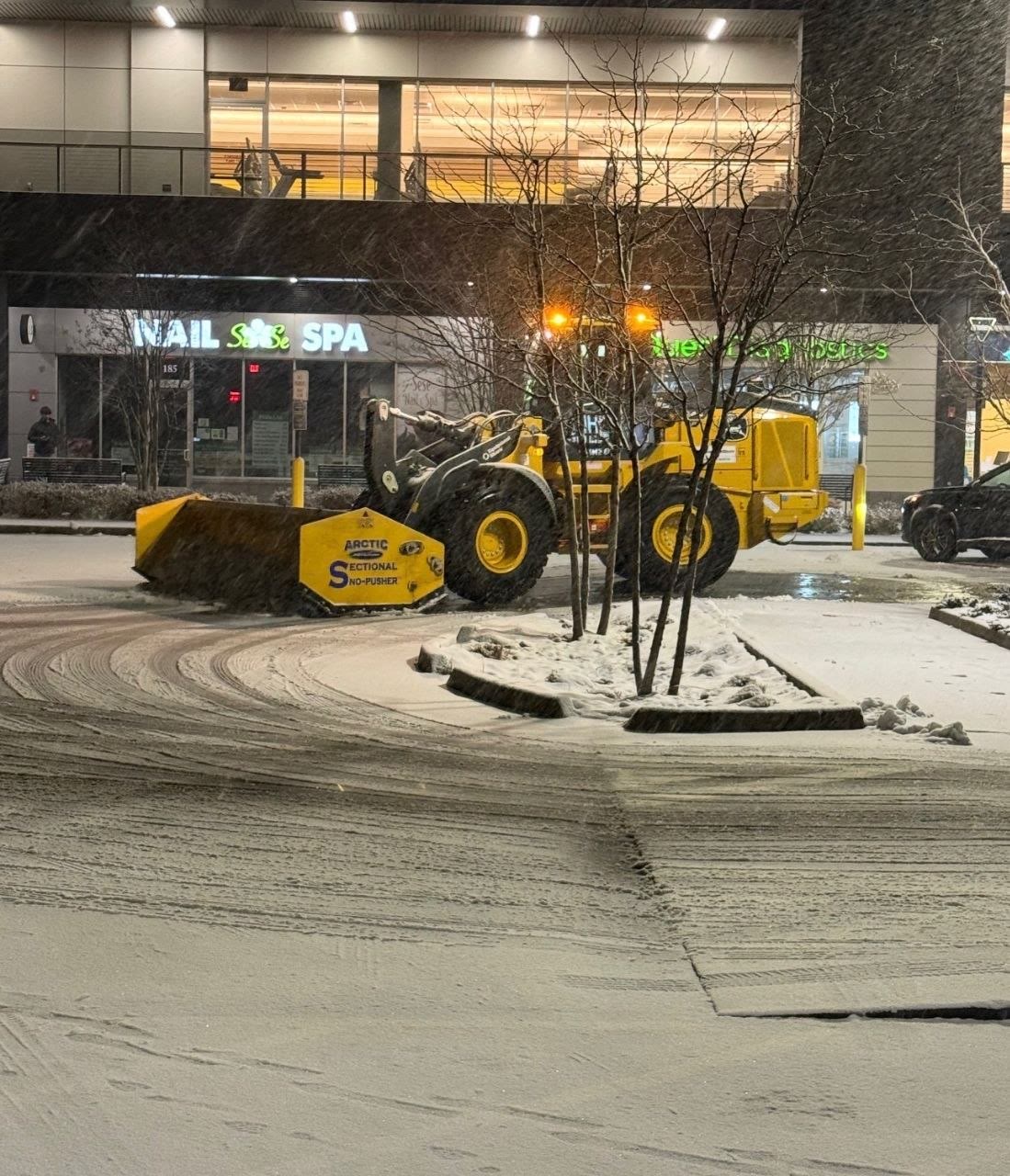 Snow pusher clearing a large retail plaza parking lot after a heavy snowstorm